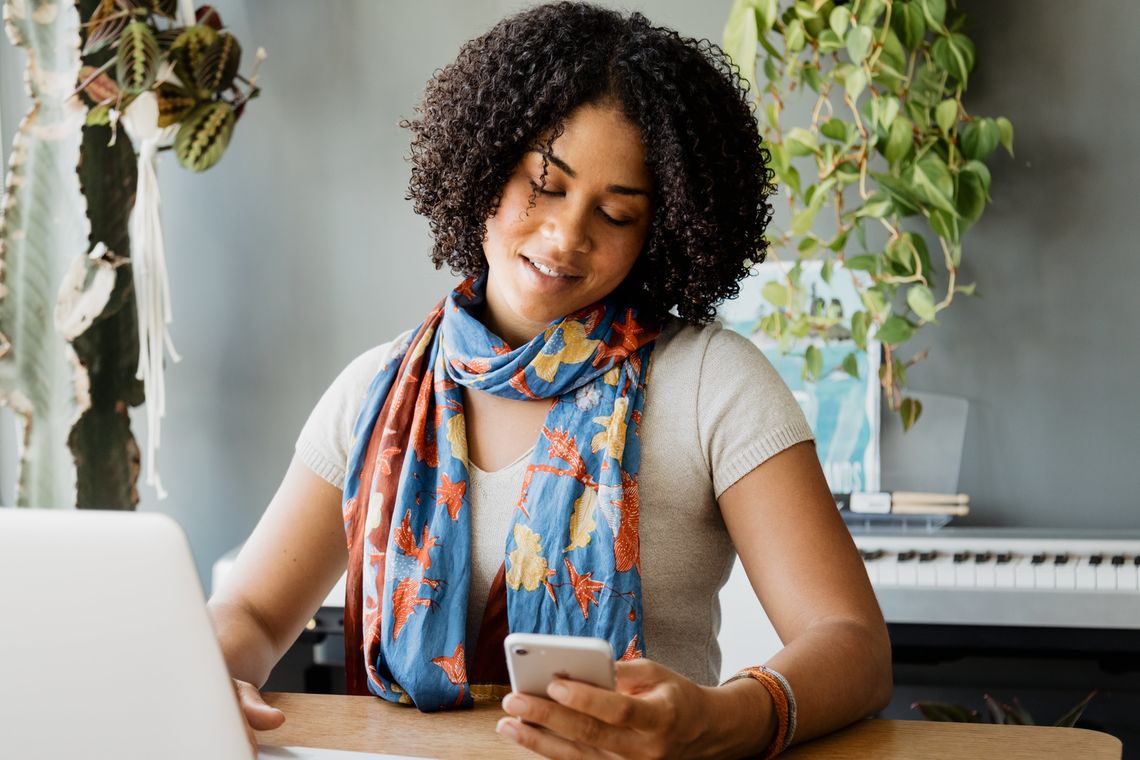 A woman sitting at a desk in front of her laptop looks at her phone