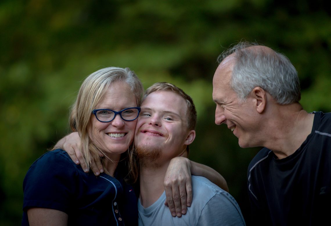 A young man with Down's syndrome hugs his parents.