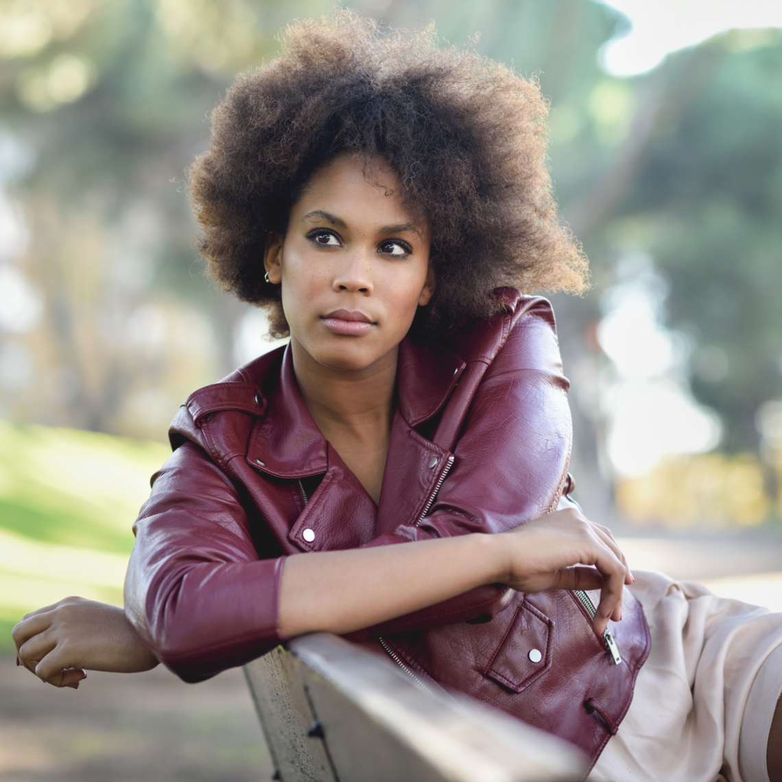 A woman is sitting on a bench outside, looking off to the side.