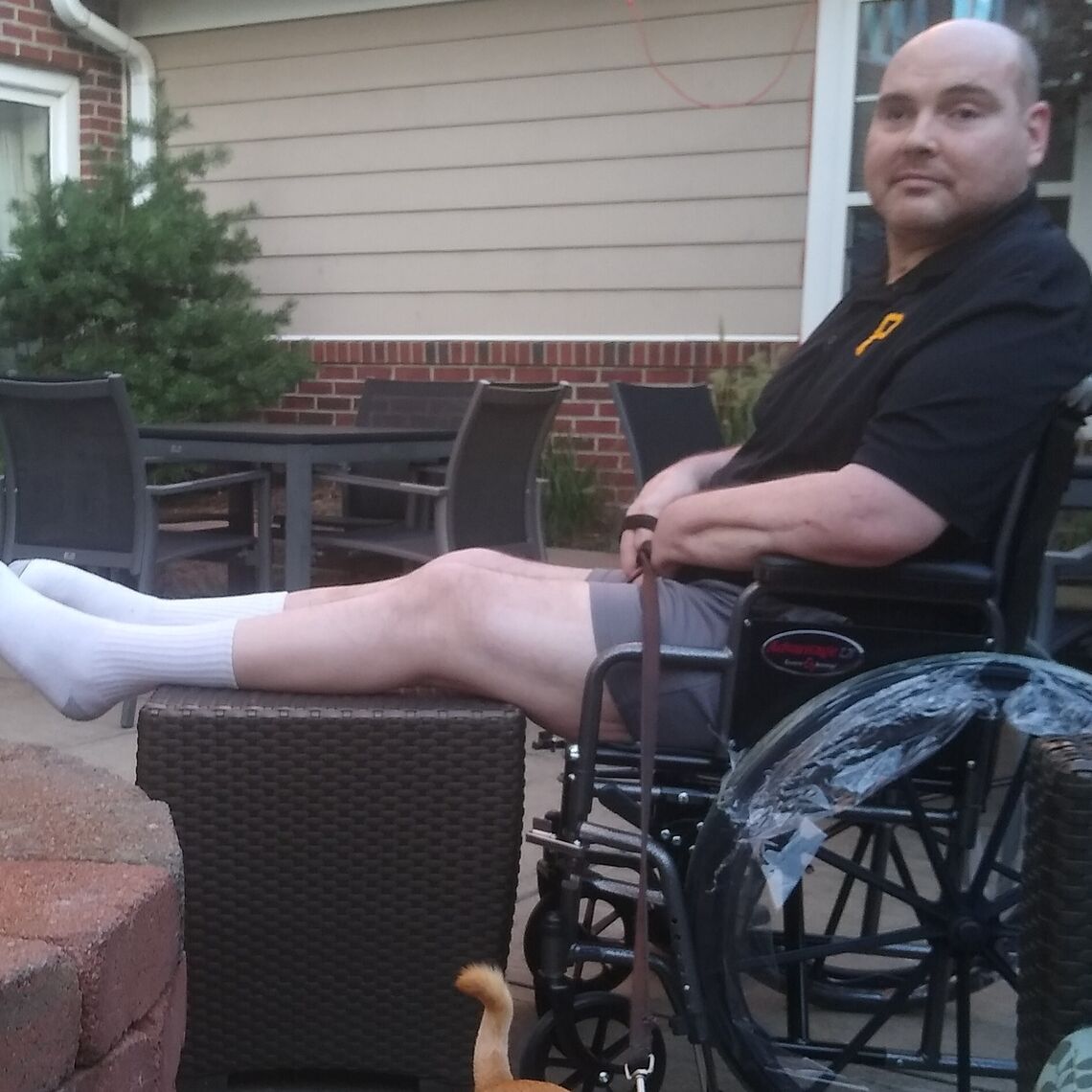 A man in a wheelchair sits on his porch with his dog