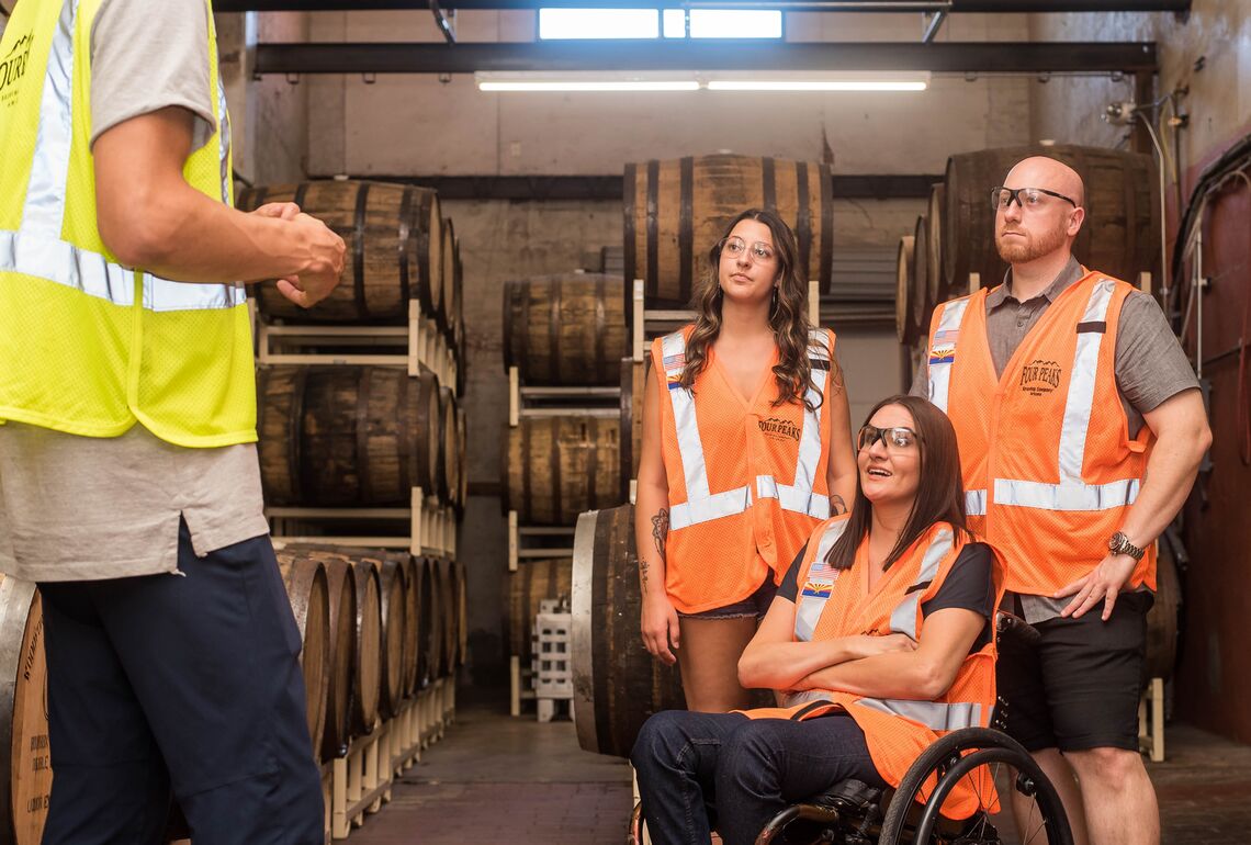 A supervisor gives instructions to three employees, all wearing reflective vests.