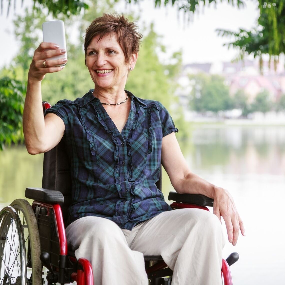 Middle aged woman in a wheelchair, taking a selfie in front of a lake