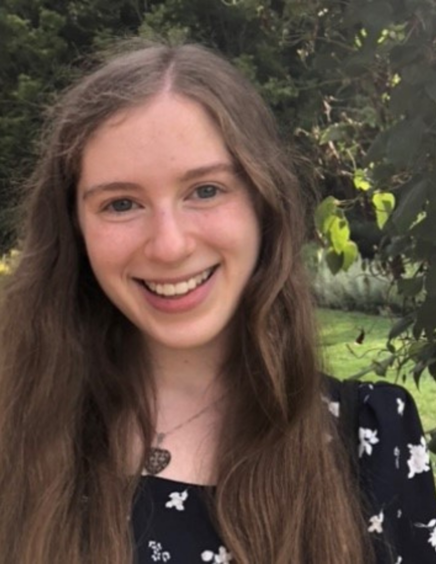 Young woman is smiling at a camera in front of a tree