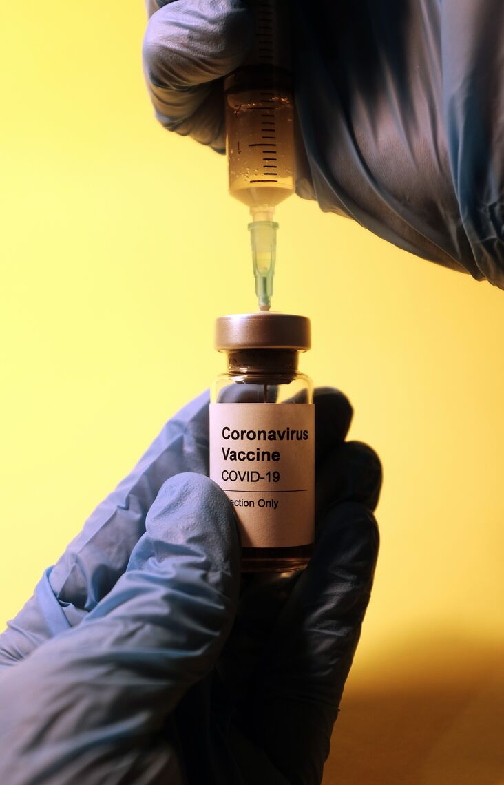 A healthcare provider holds a vial of COVID-19 vaccine and draws it into a syringe.