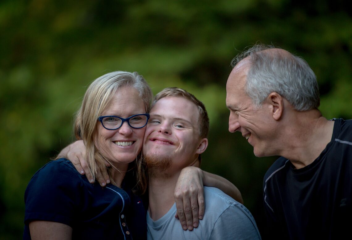 A young man with Down's syndrome and his parents smile at the camera.