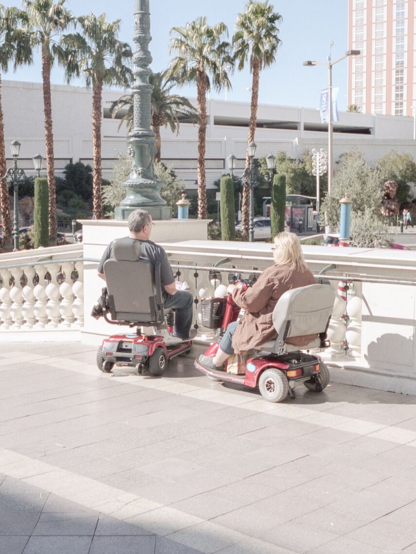 A man and a woman, both of whom are in wheelchairs, sit on a bridge and enjoy the sunny weather.