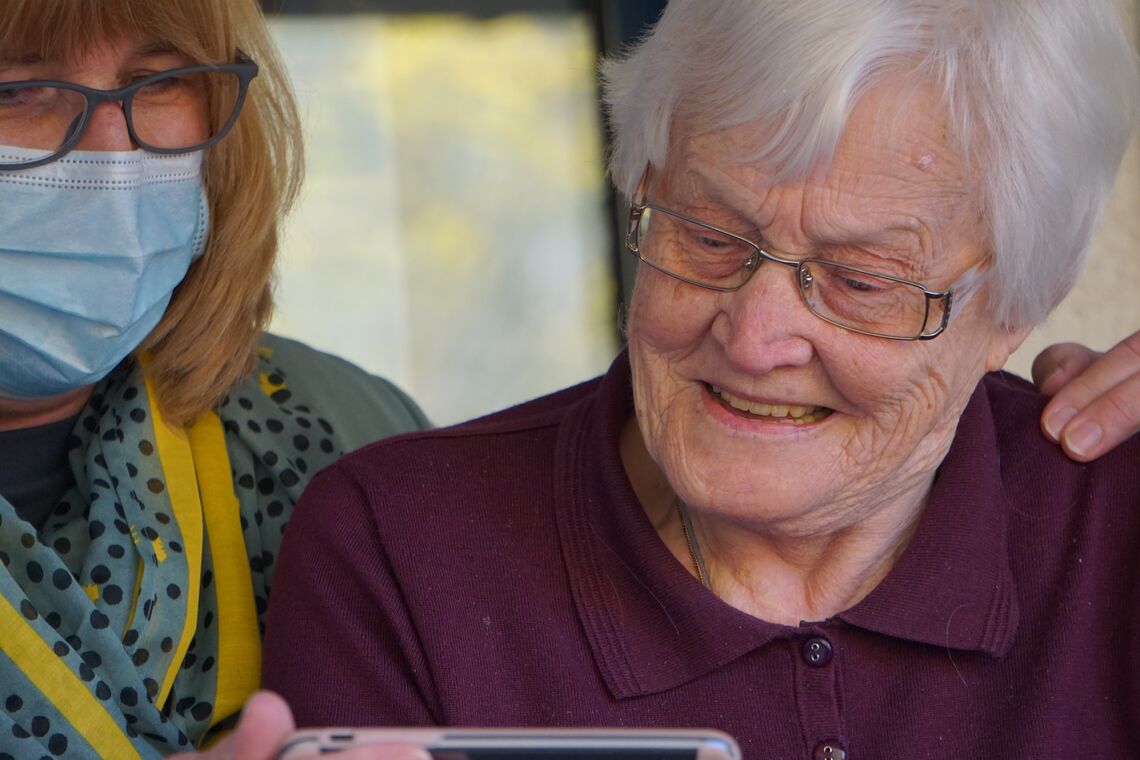 A woman shows an elderly female nursing home resident something on a phone