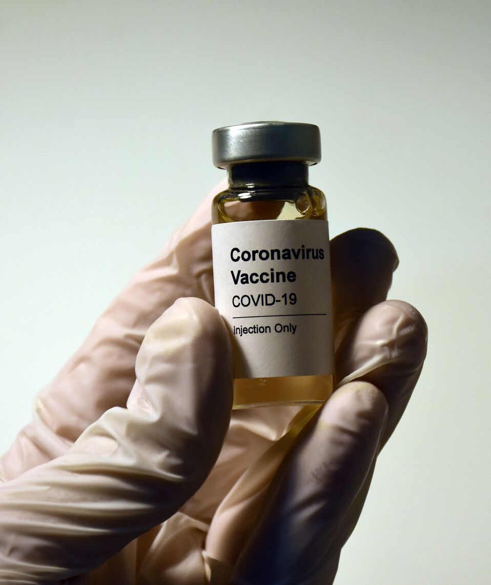 A gloved hand holds a vial of COVID-19 vaccine