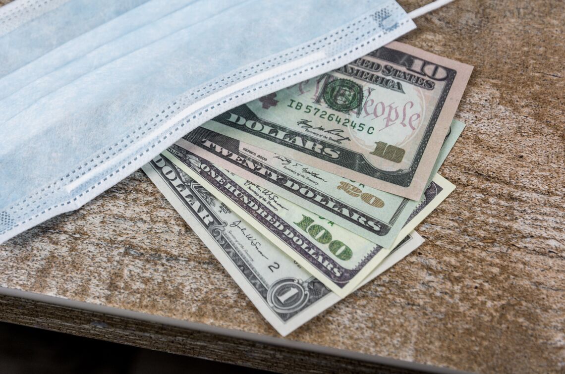 American money and a surgical mask sit on a wood table.